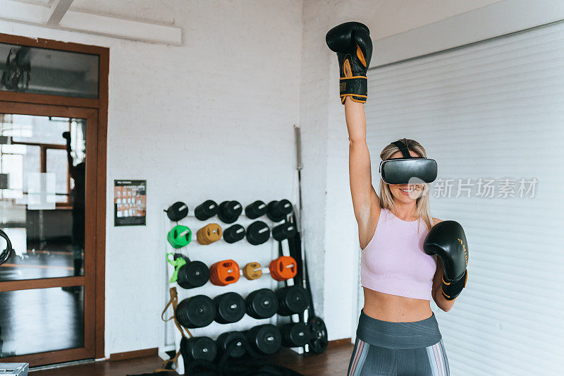 年轻的成年白人女孩穿着运动服，戴着拳击手套站在sort club举起的手，就像戴着虚拟现实耳机的赢家。健身和健康的人。